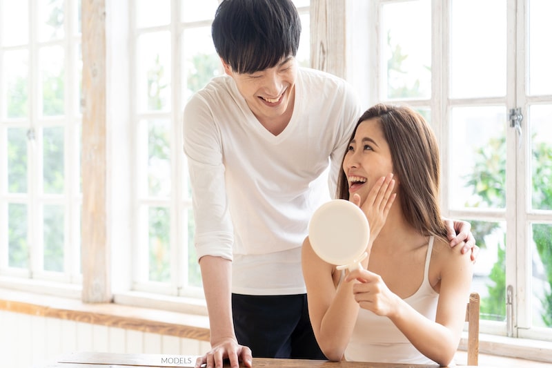 Attractive Asian couple smiling at each other, while the woman looks at her face in the mirror