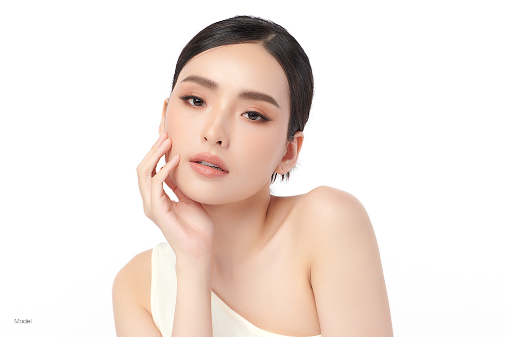 A young woman in a tan dress with her hand on her cheek